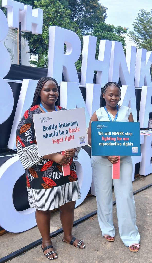 From left to right: Make Way youth representatives Elizabeth Warindi and Vilda Atieno standing and holding two signs. Warindi's sign says: 'Bodily autonomy should be a basic legal right', and Vilda's sign says: 'We will never stop fighting for our reproductive rights.'